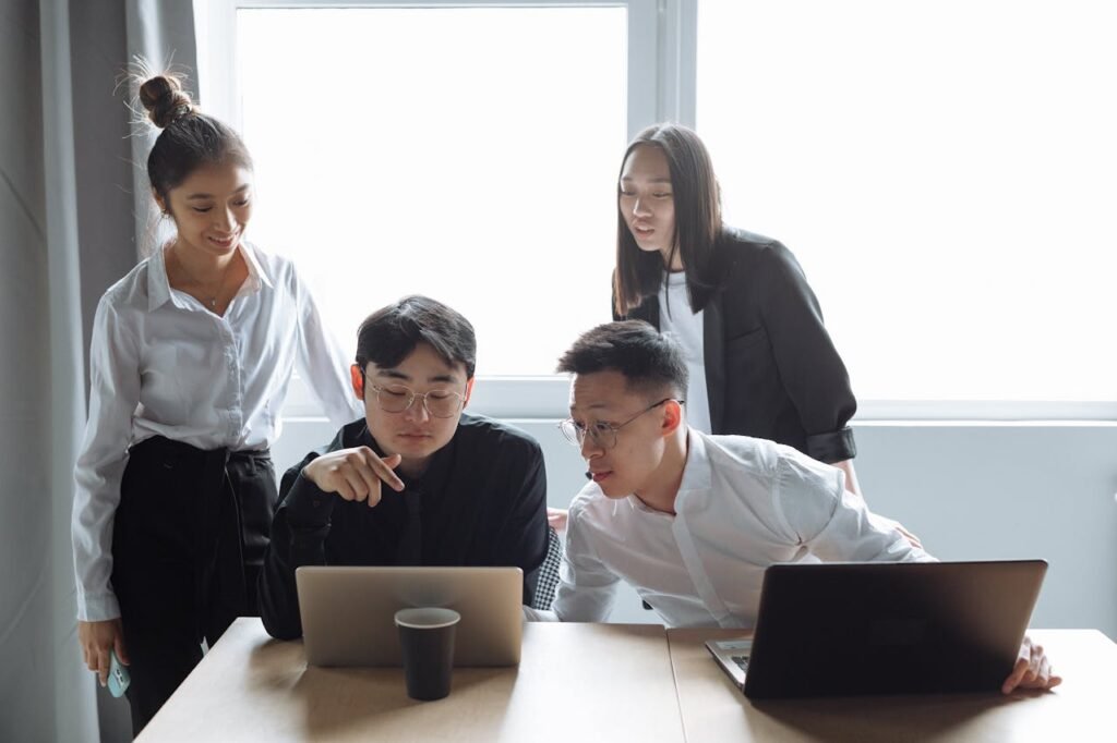 Four young professionals engaged in a collaborative meeting in an office setting with laptops.
